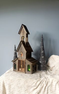 a small wooden church next to a christmas tree on a white cloth covered tablecloth