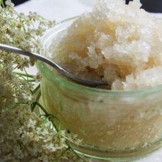 a spoon with some sugar in it on a table next to flowers and a napkin