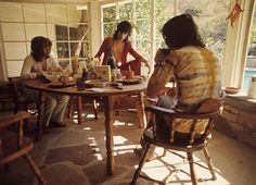 three women sitting at a table with food and drinks in front of them, looking out the window