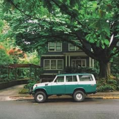 a green and white jeep parked in front of a house under a large leafy tree