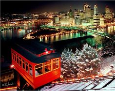 a red trolley car traveling down tracks next to snow covered trees and a city at night