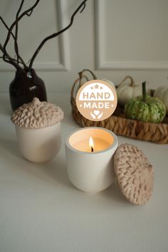 three candles sitting on top of a table next to some pumpkins and a basket