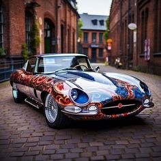 an old car is parked on the street in front of some brick buildings and cobblestones