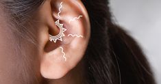 a woman wearing ear piercings with lightning and moon designs on her left behind the ear