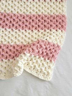 a pink and white crocheted blanket laying on top of a bed next to a pillow