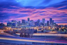 the city skyline is lit up at night with colorful clouds and light streaks in the foreground