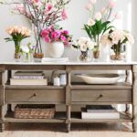 a table with flowers and vases sitting on it's sideboard in front of a window