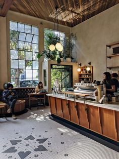 two people sitting at a counter in a coffee shop with large windows and wooden cabinets