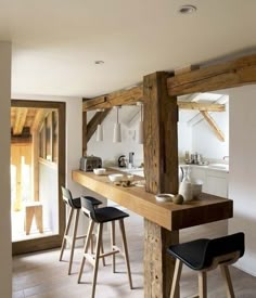 a kitchen with wooden beams and stools in front of an open door that leads to another room