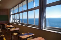 an empty classroom with tables and chairs looking out at the ocean from it's windows