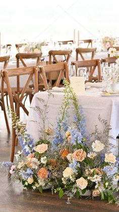 an arrangement of flowers and greenery on a table at a wedding reception with white linens