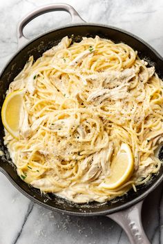 a skillet filled with chicken alfredo and lemon wedges on a marble counter top