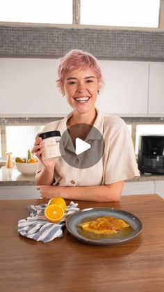 a woman sitting at a kitchen table holding a cup and plate with food on it