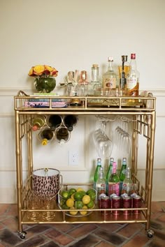 a gold bar cart filled with bottles and glasses on top of a tiled floor next to a wall