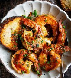 a white bowl filled with shrimp and bread on top of a wooden table next to a fork