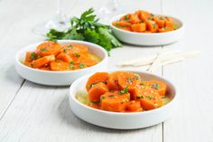 three white bowls filled with carrots sitting on top of a wooden table next to some parsley