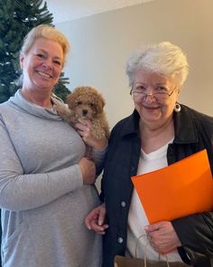 two women standing next to each other holding bags and a dog in their arms,