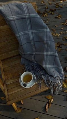 a plaid blanket and cup of tea on a wooden bench