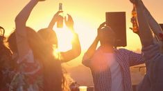 two girls are holding up their cell phones in front of the sun, while one girl is listening to music