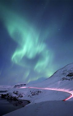 an aurora bore is seen above the snow covered hills and road in this photo, with lights streaking through the sky