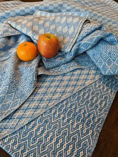 two oranges and an apple are on a blue blanket that is laying on a wooden table