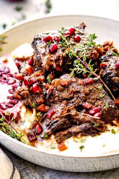 a white plate topped with meat covered in sauce and garnished with pomegranates