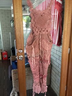 a pink crocheted dress hanging on a door