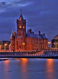 a large building with a clock on it's tower next to the water at night