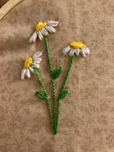 three white and yellow daisies on a piece of fabric with green stems in the middle