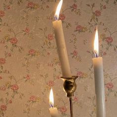 three candles are lit in front of a floral wallpaper