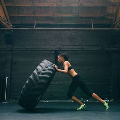 a woman pushing a large tire in an indoor gym with one leg on the ground