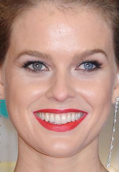 a woman with blue eyes and red lipstick smiles at the camera while wearing large earrings