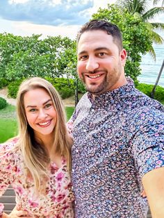 a man standing next to a woman on top of a wooden bench near the ocean