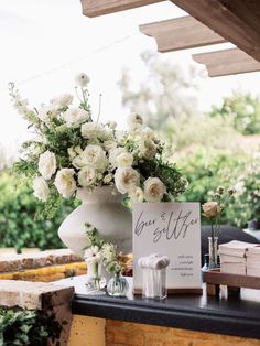 a vase with white flowers sitting on top of a table next to a sign that says love is life