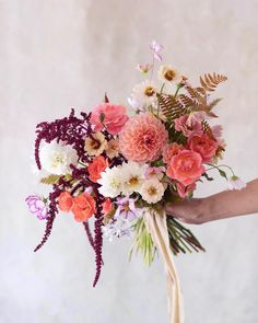 a person holding a bouquet of flowers in their hand with pink, white and orange colors