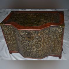 an old wooden box with ornate designs on it's sides and lid is sitting on a white sheet