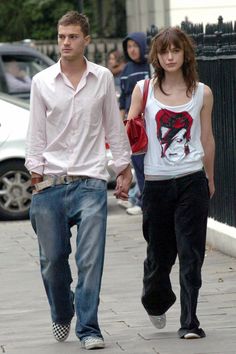 two people walking down the street with one person wearing jeans and a white shirt on