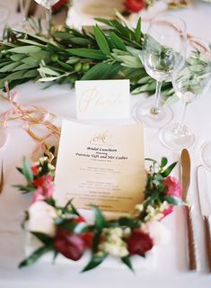 the table is set with white and red flowers, greenery, and menu cards