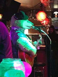 a man in a bear suit playing guitar and singing into a microphone at a bar