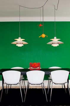 a dining room with green walls and white chairs in front of a black table surrounded by hanging lights