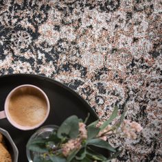 a cup of coffee and some cookies on a black plate next to a vase with flowers