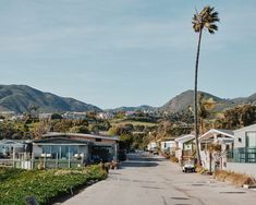 a street lined with houses and palm trees in front of some mountain range behind them