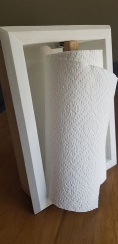 a roll of toilet paper sitting inside of a white frame on top of a wooden table