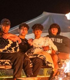 four young men sitting next to each other on a bench in front of a tent