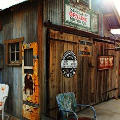 an old outhouse with chairs and signs on the side of it in front of a building