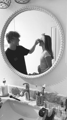 a boy and girl are brushing their hair in the bathroom mirror while looking at each other's reflection