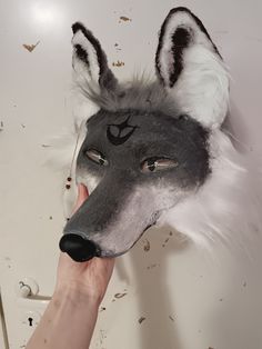 a wolf mask being held up to the camera by someone's hand in front of it