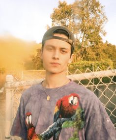 a young man standing in front of a fence with a parrot on it's t - shirt