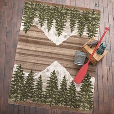 an area rug with trees and mountains in the middle on a wooden floor next to a red spoon