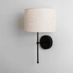 a black wall light with a white shade on it's face and a round lamp hanging from the side